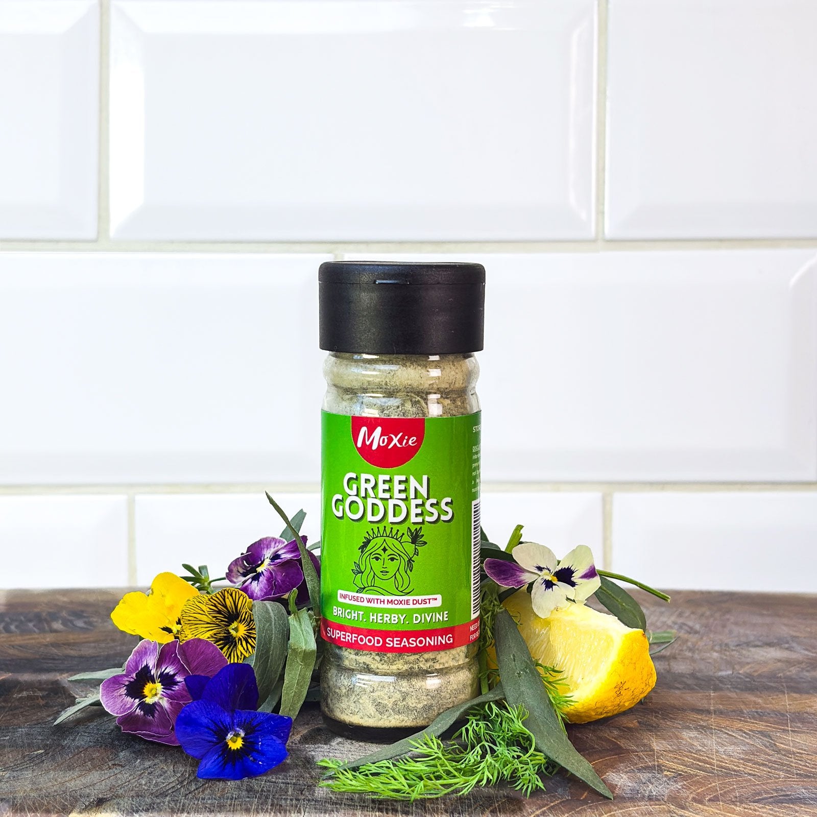 Moxie Green Goddess Superfood Seasoning bottle with fresh herbs and lemon on kitchen counter