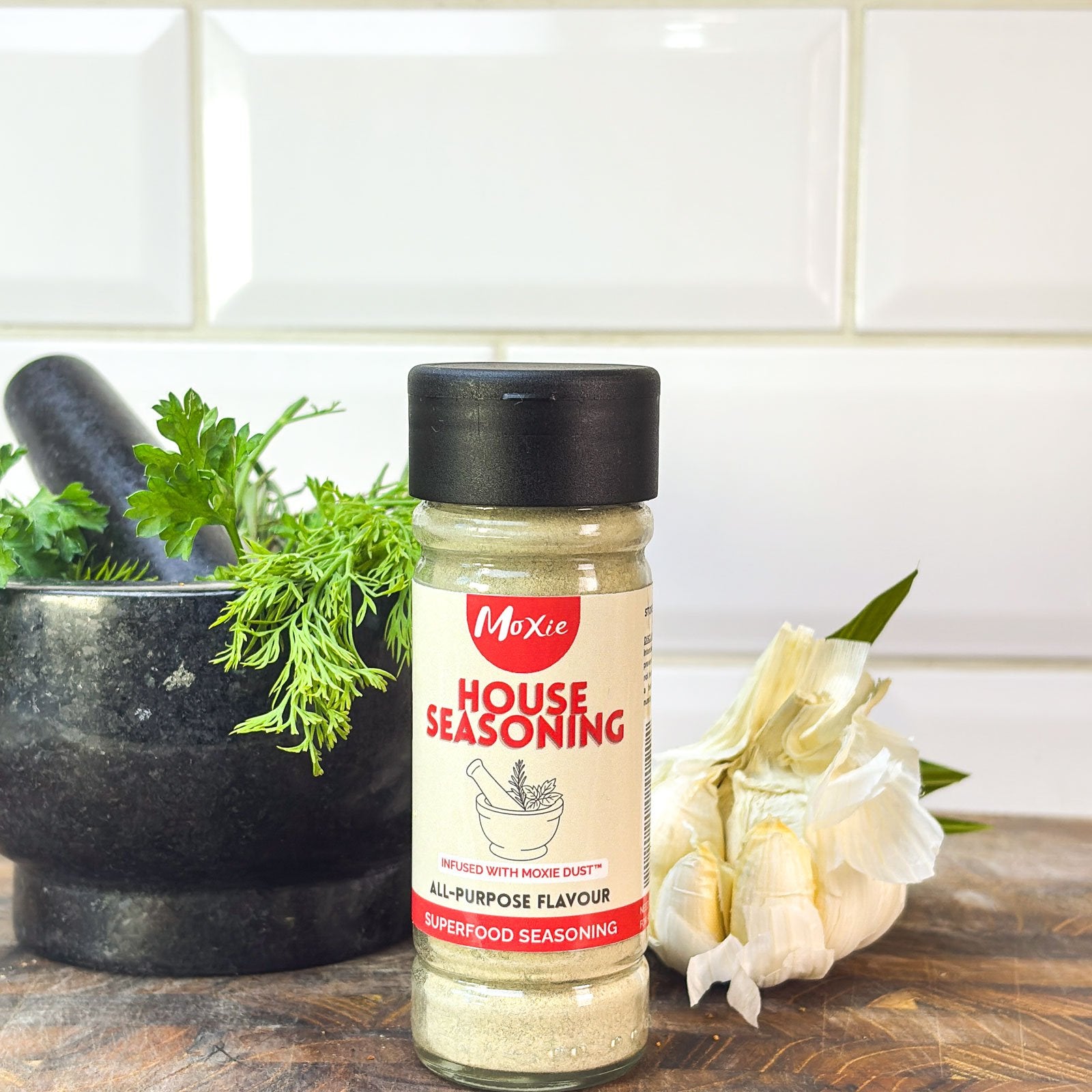Moxie House Seasoning bottle next to pestle and mortar and garlic on white tile kitchen background
