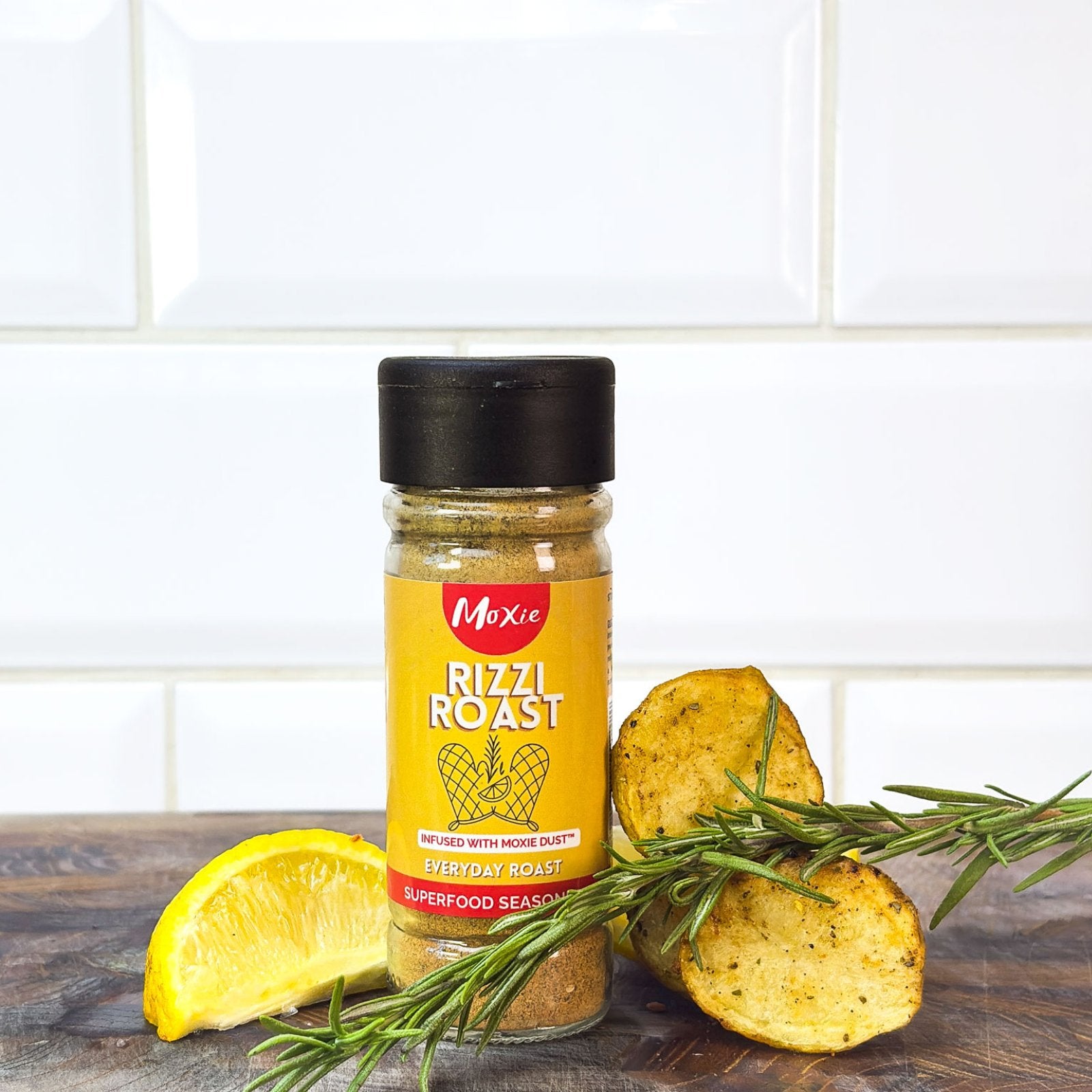 Moxie Rizzi Roast Superfood Seasoning bottle with roast potato, lemon slices and rosemary sprigs